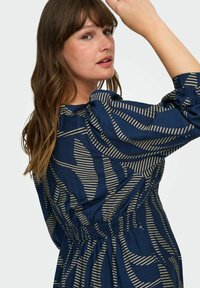 Vestido azul marino con patrón de rayas beige, con cintura recogida y mangas abullonadas, hecho de tejido ligero.