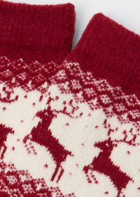Red and cream knitted socks featuring a reindeer pattern, with a soft texture and ribbed cuffs. Accents of white throughout the design.