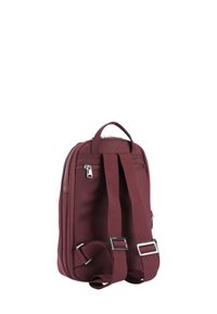 Maroonfärgad tygryggsäck med ett handtag upptill och justerbara axelremmar. Har ett zippered utrymme och silverfärgade detaljer.