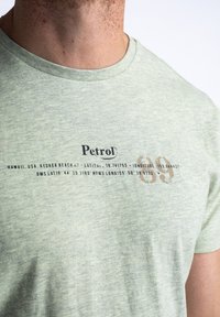 Green heathered cotton t-shirt with round neckline. Features printed text and coordinates in black, with a faded brown accent on the number 09.
