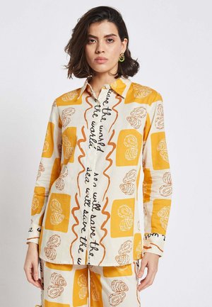 Lightweight button-up shirt in cream with yellow and brown abstract floral patterns and handwritten text; long sleeves and a classic collar.
