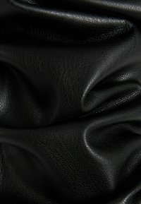 Černá kožená tkanina s texturovaným povrchem a jemnými záhyby a drapériemi, které ukazují hloubku a rovnoměrný vzor struktury.