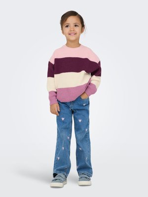 Strikkegenser med mønster i rosa, hvitt og lilla striper; kombinert med lyseblå jeans med hjerteprint; grå sko.