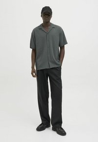 Camisa de botones de manga corta en gris oscuro con textura, combinada con pantalones holgados negros y gorra negra. Material suave, corte relajado.