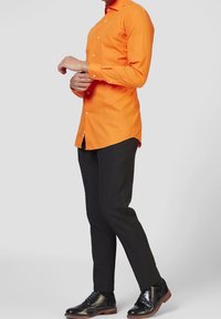 Pomarańczowa koszula z guzikami, dopasowana, w połączeniu z czarnymi spodniami slim-fit i czarnymi butami eleganckimi. Gładki materiał, dopasowany krój.