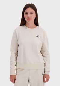 Felpa beige a girocollo realizzata in morbido tessuto, con un piccolo logo di coniglio nero sul lato sinistro del petto e polsini e orlo a coste.