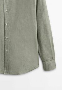 Chemise à manches longues vert olive clair avec poignets boutonnés, montrée de la partie médiane à l’extrémité de la manche sur fond blanc.