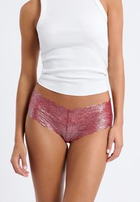 Culottes de encaje en un tono rojo profundo, con bordes ondulados y un patrón floral, combinados con una camiseta ajustada blanca.