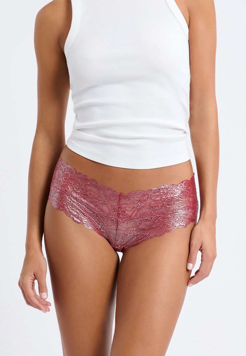 Culottes de encaje en un tono rojo profundo, con bordes ondulados y un patrón floral, combinados con una camiseta ajustada blanca.