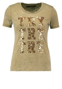 T-shirt verde oliva con maniche corte e scollatura rotonda, caratterizzato da testo in paillettes dorate "TRY" ripetuto più volte sulla parte anteriore.