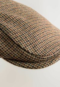 Vlněná plochá čepice s texturovaným vzorem houndstooth v hnědých, zelených a béžových tónech. Zaoblený tvar s mírně zdviženým okrajem.