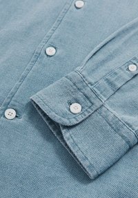 Lichtblauw denim shirt met een spitse kraag, witte knopen en een omgeslagen manchette, dat een gestructureerde stof laat zien met een subtiel weefpatroon.