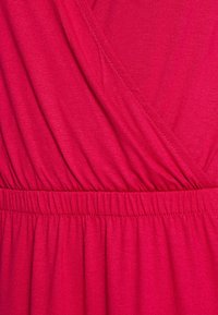 Gros plan sur un tissu rose vif avec une taille froncée et des coutures diagonales créant des plis et une texture douce.