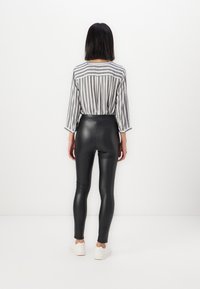 Gestreepte grijs-witte top met driedelige mouwen, gecombineerd met zwarte faux leren leggings en witte sneakers. Effen witte achtergrond.