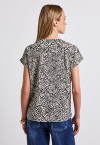 Top à manches courtes, ample, arborant un imprimé zèbre noir et blanc sur fond beige, confectionné dans un tissu léger.