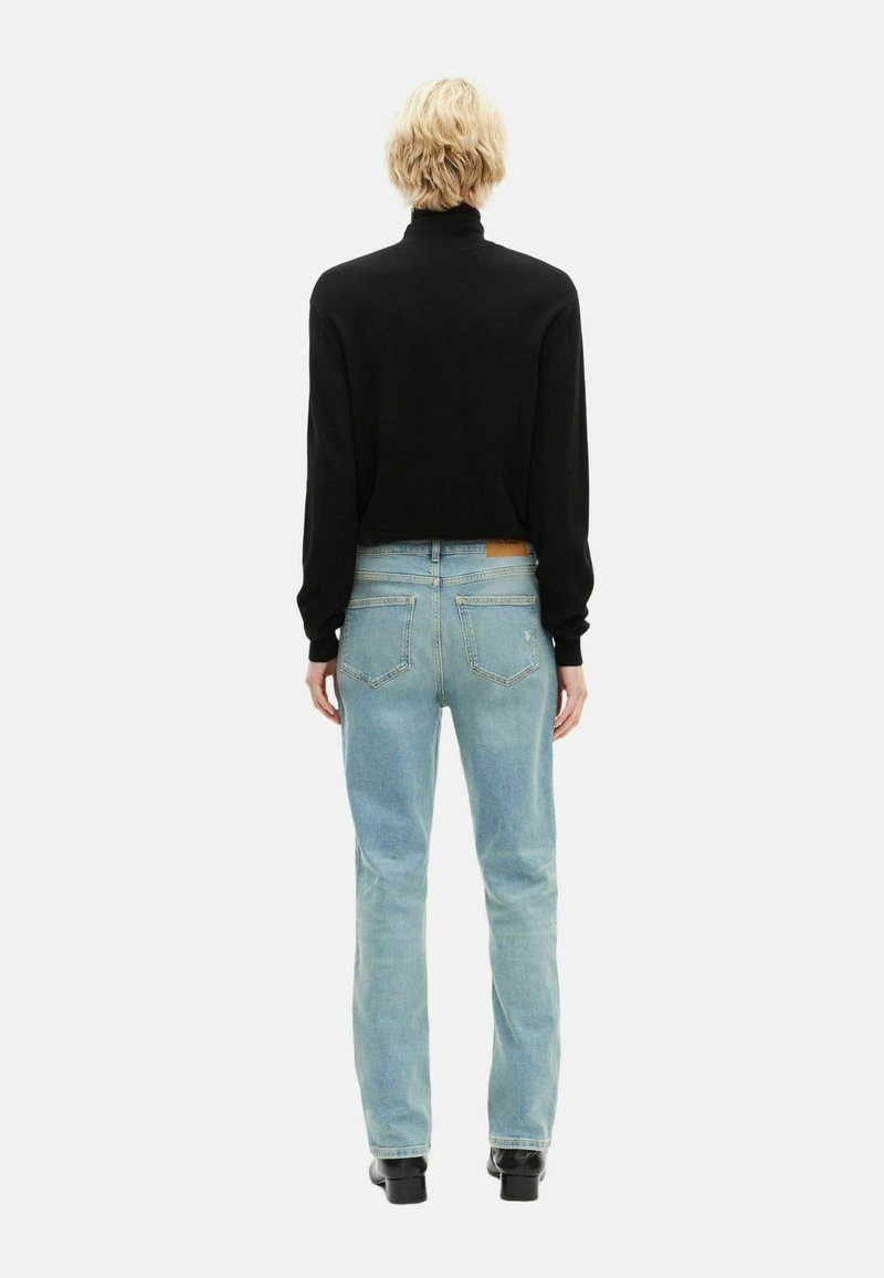Cropped black turtleneck sweater paired with light blue jeans, featuring back pockets and a leather tag on the waistband. Black ankle boots.