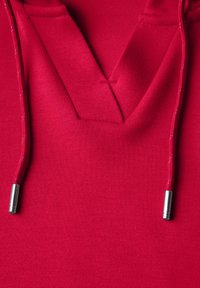 Hoodie rouge avec un design en V, cordons avec embouts métalliques et un tissu lisse et texturé.