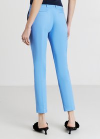 Hellblaue, maßgeschneiderte Hose mit schmaler Passform, dezenten Gesäßtaschen und kombiniert mit schwarzen, hochhackigen Mules mit floralen Akzenten.