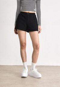 Juodi medvilniniai šortai su laisvu siluetu, puošti Calvin Klein logotipu ant juosmens. Derinami su baltais platforminiais sportbačiais ir stori daiktais.