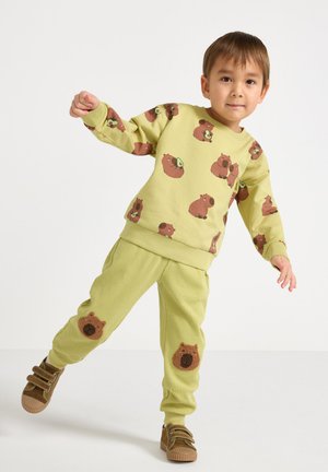 Felpa di cotone verde chiaro con stampe di orsi marroni, abbinata a pantaloni coordinati con trama e toppe a forma di orso sulle ginocchia. Scarpe marroni.