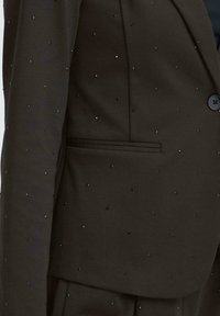 Must الأسود tekstuuriga bleiser väikeste mustade helmestest kaunistustega ja esise nööbiga sulgemisega.