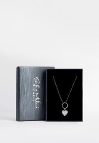 Ciondolo a forma di cuore in argento con cristalli su una catena all'interno di una scatola per gioielli nera aperta con coperchio grigio testurizzato.