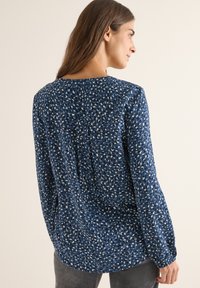 Chemise à manches longues bleu marine avec un motif floral texturé dans des teintes de bleu clair et foncé, dotée d'un col rond et d'une coupe ample.