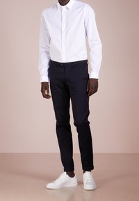 Witte blouse met lange mouwen, gecombineerd met donkerblauwe slim-fit broek en witte sneakers, wat een schone en moderne esthetiek tentoonstelt.