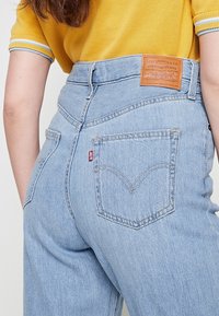 Jeans de tiro alto de color azul claro, hechos de denim, que cuentan con una etiqueta de cuero marrón, bolsillos traseros con detalle de costura y un corte relajado.