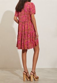 Rosa kortärmad klänning med ett blomstergeometriskt mönster, volangkant och avslappnad passform, bärs tillsammans med bruna platåsandaler med träklackar.