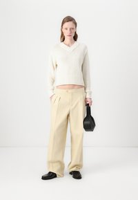 Pull en crème tricoté avec un col en V, associé à un pantalon large beige clair. Les accessoires comprennent un sac à main noir et des mocassins.