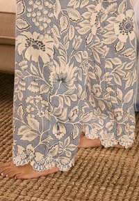 Flowy blue fabric with white floral patterns, featuring a scalloped lace hem. Texture is soft, designed for comfort and breathability.