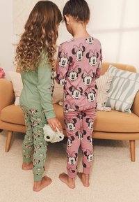 Two children face away, wearing matching long-sleeve pajamas. One is mint green with patterns, the other pink with Minnie Mouse designs.