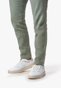 Sneakers bianchi in pelle con texture, suola spessa e accenti beige, abbinati a pantaloni fitted verde chiaro in un tessuto morbido.