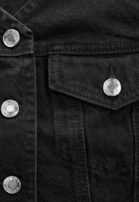 Schwarzer Denim-Stoff mit sichtbarer Tasche, silbernen Druckknöpfen und kontrastierenden Nähten. Glatte Textur und strukturiertes Design.