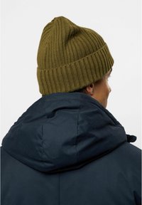 Cappello a coste verde oliva indossato con un giubbotto imbottito blu navy, caratterizzato da un cappuccio strutturato e una superficie liscia del tessuto del giubbotto.
