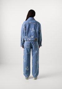 Veste en denim et pantalon large en bleu clair, ornés de motifs imprimés blancs. Le tissu a une texture classique avec fermeture à boutons et poches.