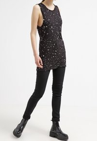 Svart ärmlös topp med ett prickigt vitt mönster, kombinerad med åtsittande svarta jeans och kraftiga svarta plattformsskor. Enkel, modern design.