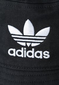 Cappellino da baseball nero con logo Adidas ricamato bianco che presenta tre strisce e il design del trifoglio sul davanti. Texture del tessuto liscia.