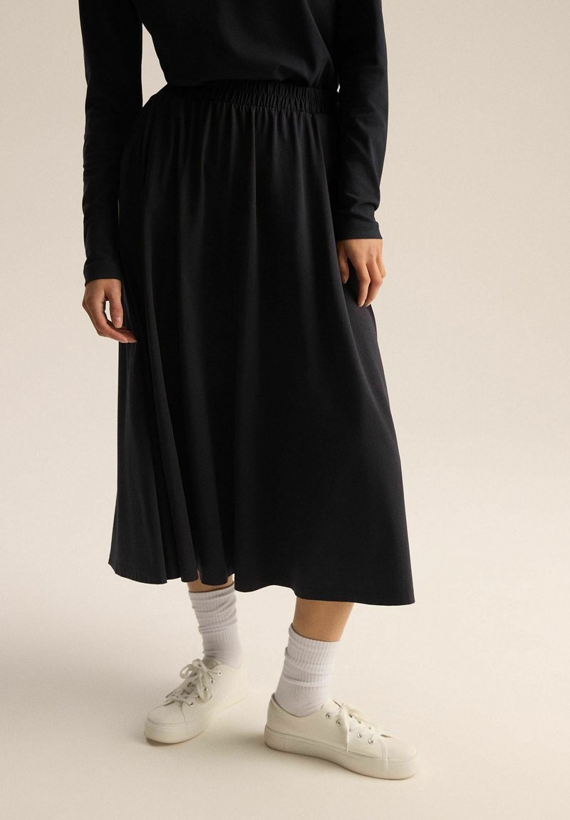 Czarna spódnica o długości kostek z elastycznym paskiem w talis, o gładkiej strukturze. Zestawiona z białymi trampkami i skarpetkami.