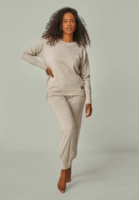 Beiges gestricktes Loungewear-Set, bestehend aus einem langärmeligen Oberteil mit gerippten Bündchen und einer Hose mit Kordelzug und elastischen Knöchelöffnungen.