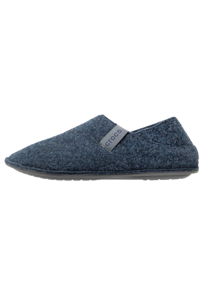 Zapato de lana de fieltro tipo slipper en azul marino con punta afilada, parte trasera redondeada y una etiqueta de logo gris. Presenta un exterior texturizado y suela de goma.