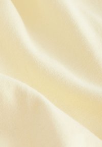 Měkká krémová látka s jemnou pletenou texturou a jemnými záhyby vytvářejícími hladké vlny a stíny.