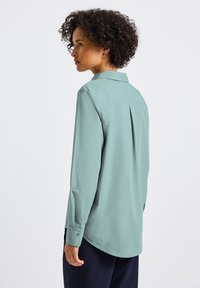 Camicia a maniche lunghe verde menta con colletto, dettaglio a pieghe nella parte posteriore e polsini con bottoni. Tessuto morbido e vestibilità rilassata.