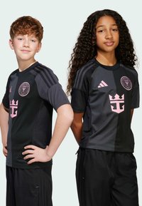 Jugendfußballtrikots in Schwarz mit rosa Akzenten, die ein diagonales Farbblockdesign, das Team-Logo und eine Dreistrich-Schultergestaltung aufweisen.