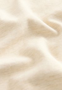 Vaaleanbeige kangas, jossa on pehmeä ja sileä pinta, hienovarainen kudottu kuvio ja lievä jousto luoden pehmeitä laskoksia ja aaltomaisia muotoja.