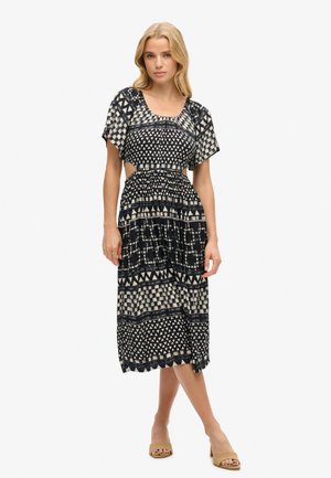 Maxi dress in black and cream with geometric patterns, short sleeves, elastic waist, mid-calf length, and side cutouts above the waist.
