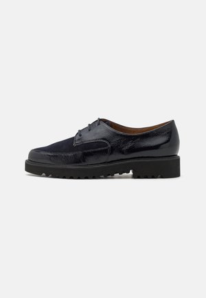 Chaussure à lacets en cuir noir et daim avec semelle épaisse à rainures, talon bas et bout arrondi lisse, photographiée de profil sur fond blanc.