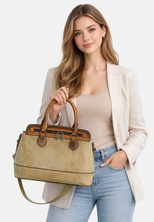 Jonge vrouw in een beige blazer en blauwe jeans houdt een lichtbruine suède handtas met bruine leren handgrepen vast, licht glimlachend tegen een witte achtergrond.
