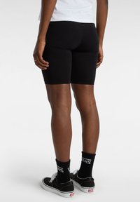 Shorts de bicicleta negros, material elástico, longitud hasta la mitad del muslo, combinados con zapatillas Vans negras y calcetines crew negros con un logo blanco.